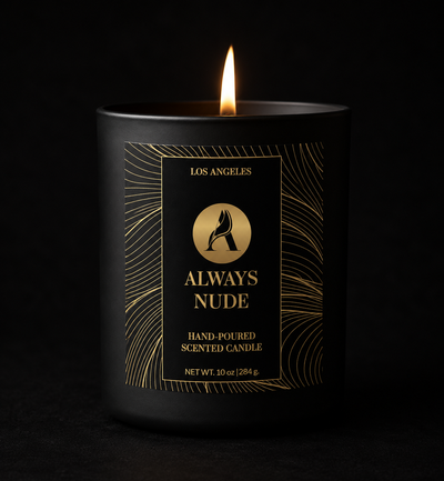 Always Nude luxury hand-poured candle in a matte black jar with gold foil label, lit on a marble surface.
